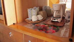 Una kitchenette con una cafetera, un cesto de pan y una bandeja con frutas.