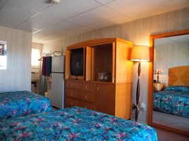 Habitación de hotel con dos camas, un aparador de madera, un espejo y una pequeña kitchenette.