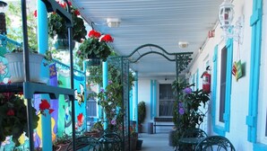 Un espacio de estar al aire libre cubierto con mesas y sillas de metal, rodeado de macetas con plantas y flores.