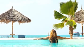 Una persona descansando en una piscina con vista al océano y palmeras.