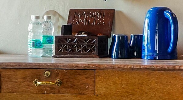 Une commode en bois avec une poignée de tiroir en laiton, une bouteille d’eau, une boîte portant l’inscription « KARIBU SMILES » et une bouilloire bleue.
