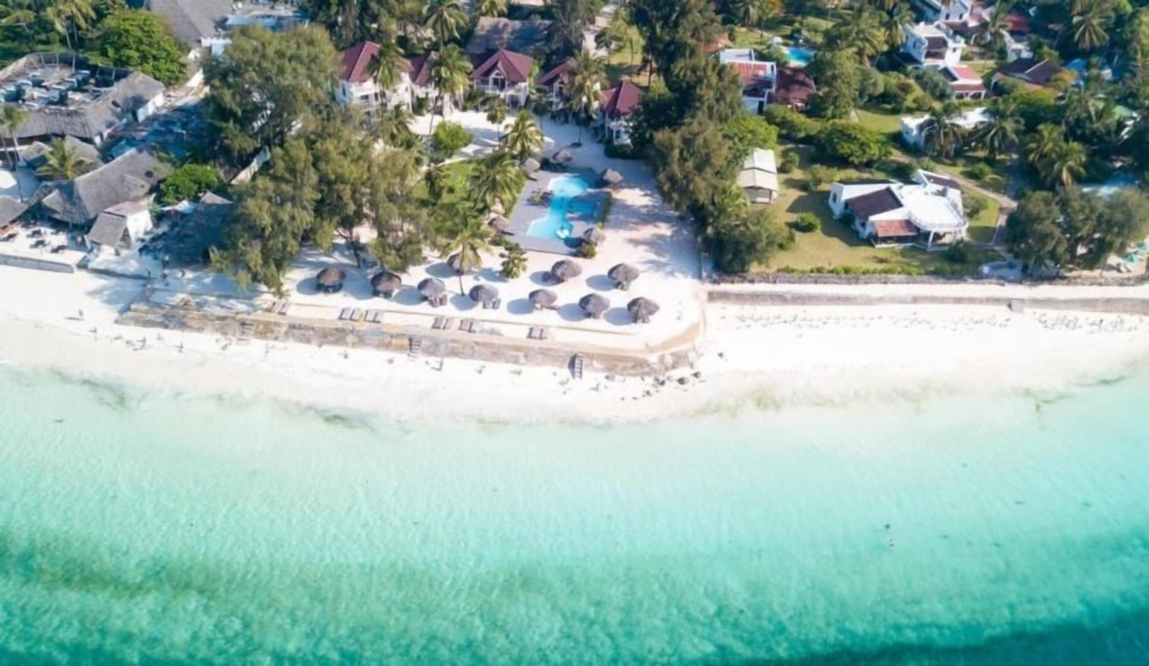 An aerial view of a coastal resort with a beach, swimming pool, and multiple villas.
