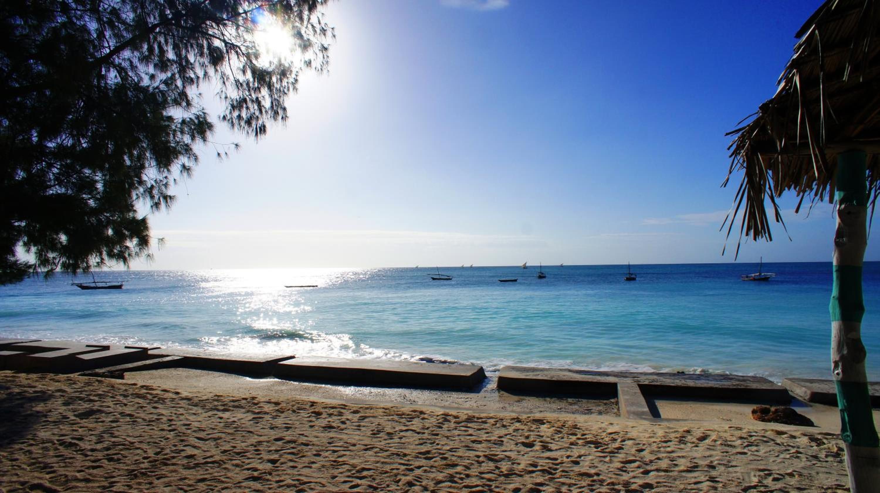 Una playa con cielo despejado, mar tranquilo y barcos.
