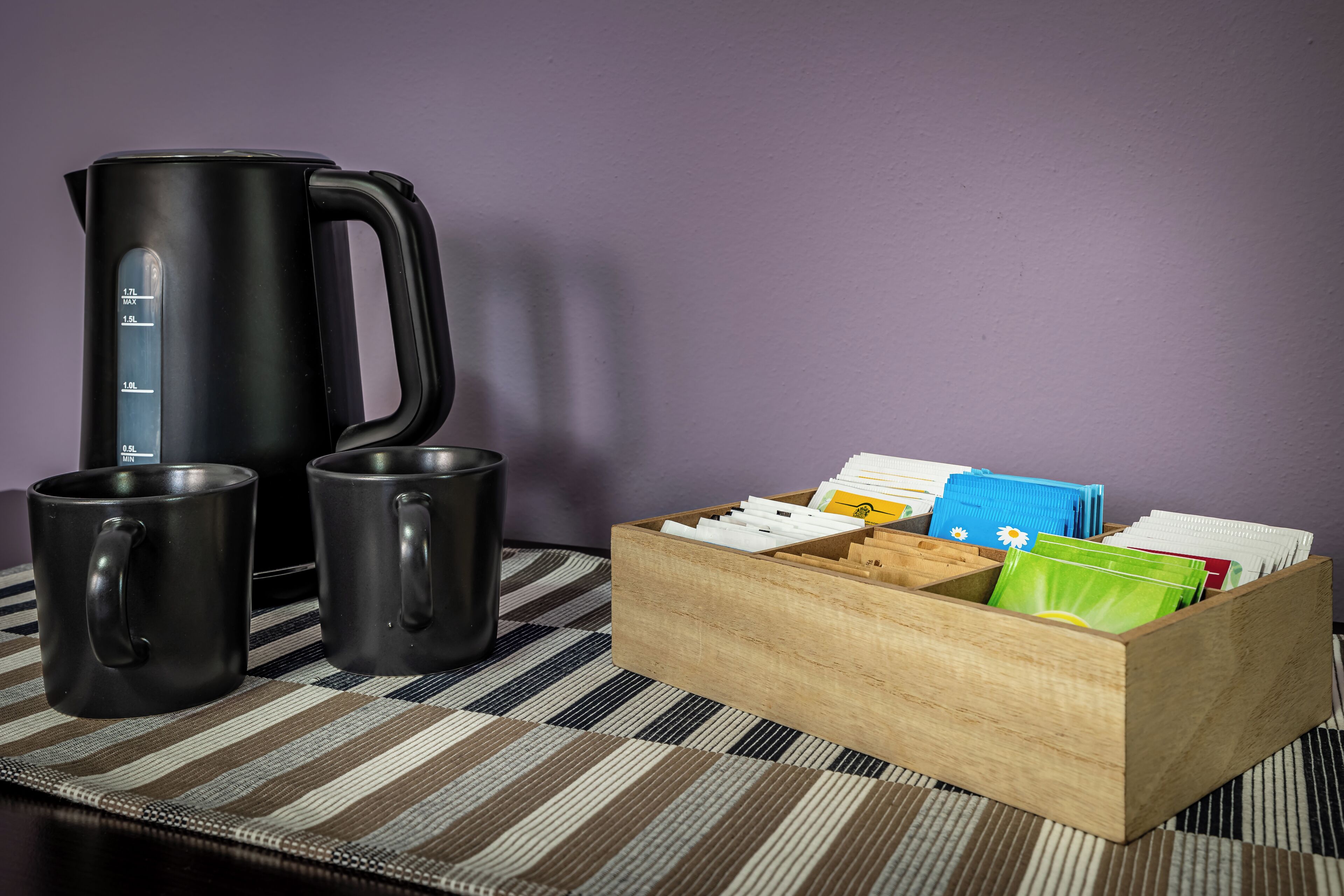 A kitchen area with a black kettle, two black mugs, and a wooden box containing various items.