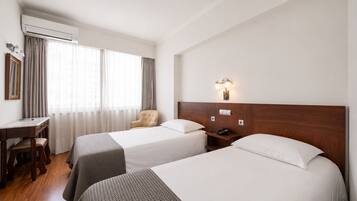 Quarto de hotel com duas camas, uma escrivaninha, uma cadeira e mesa de cabeceira com telefone.