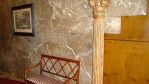 Una pared de mármol con un cuadro enmarcado, un banco de madera y una columna.