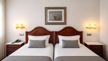 A double room with two beds, bedside lamps, a framed picture on the wall, and a telephone on the nightstand.