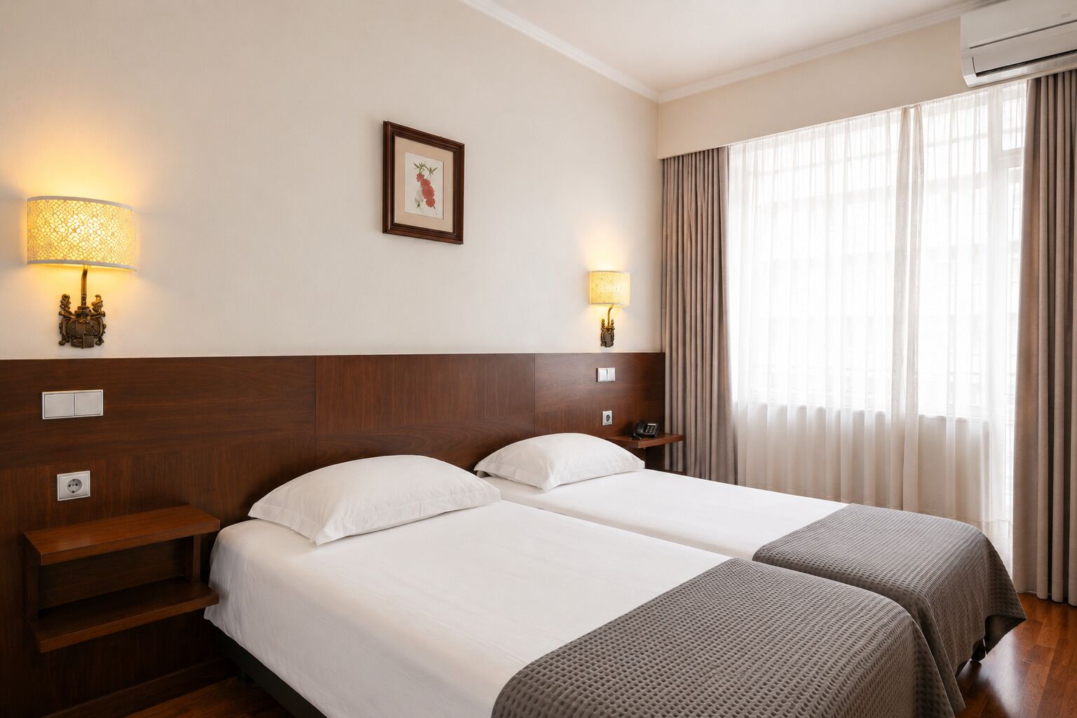 Habitación de hotel con dos camas, lámparas de noche, un cuadro en la pared y un equipo de aire acondicionado.