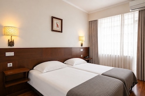 Habitación de hotel con dos camas, lámparas de noche, un cuadro en la pared y un equipo de aire acondicionado.