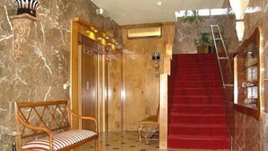 Un vestíbulo con alfombra roja, un banco de madera, una escalera y paredes de mármol.