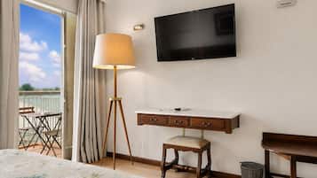 Habitación de hotel con cama, escritorio, silla, lámpara de pie, televisión y balcón con sillas.