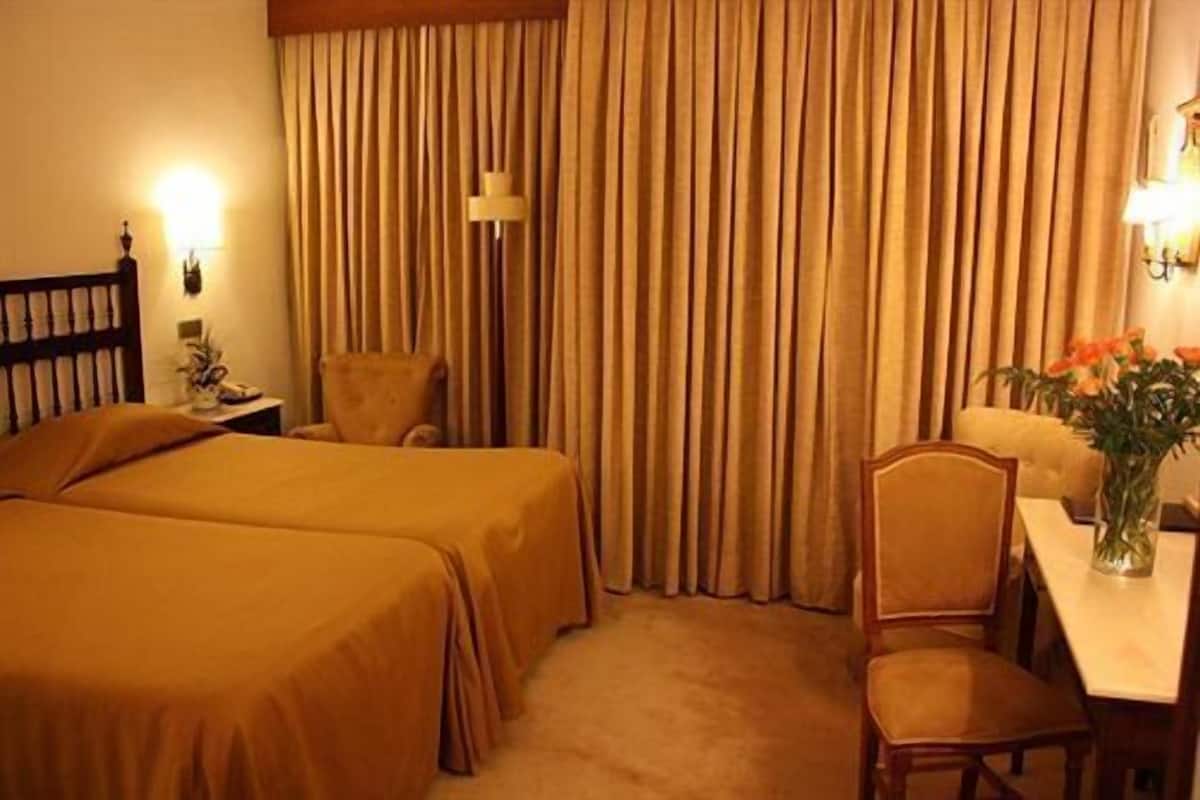 Une chambre d’hôtel avec deux lits, un bureau, une chaise, une lampe et un rideau.