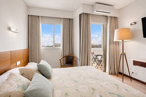 Quarto de hotel com cama, cadeira, mesa, abajur e vista para o exterior.
