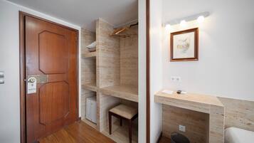 Un pasillo con una puerta de madera, un pequeño rincón de descanso y un aplique en la pared.