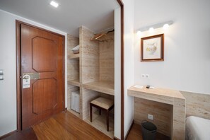 Um corredor com porta de madeira, um pequeno espaço para sentar e um aplique.