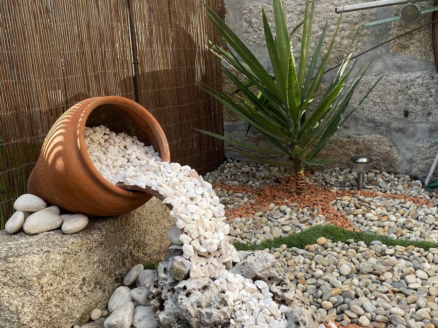 Um jardim com cerca de bambu, um vaso de terracota e diversos seixos.