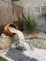 A garden with a bamboo fence, a terracotta pot, and a variety of pebbles.