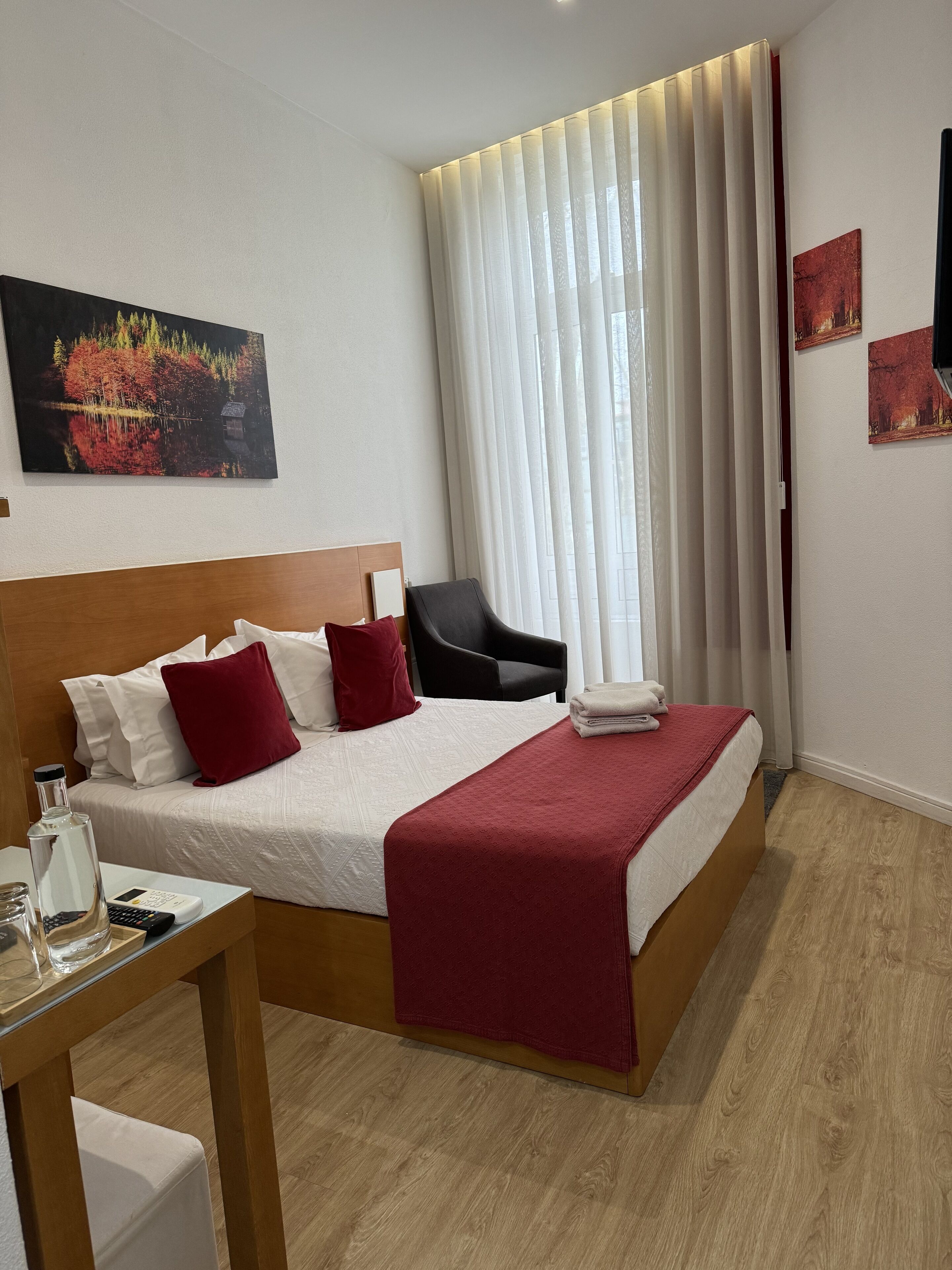 Een hotelkamer met een bed, een stoel, een tafel met een fles en glazen, en een schilderij aan de muur.