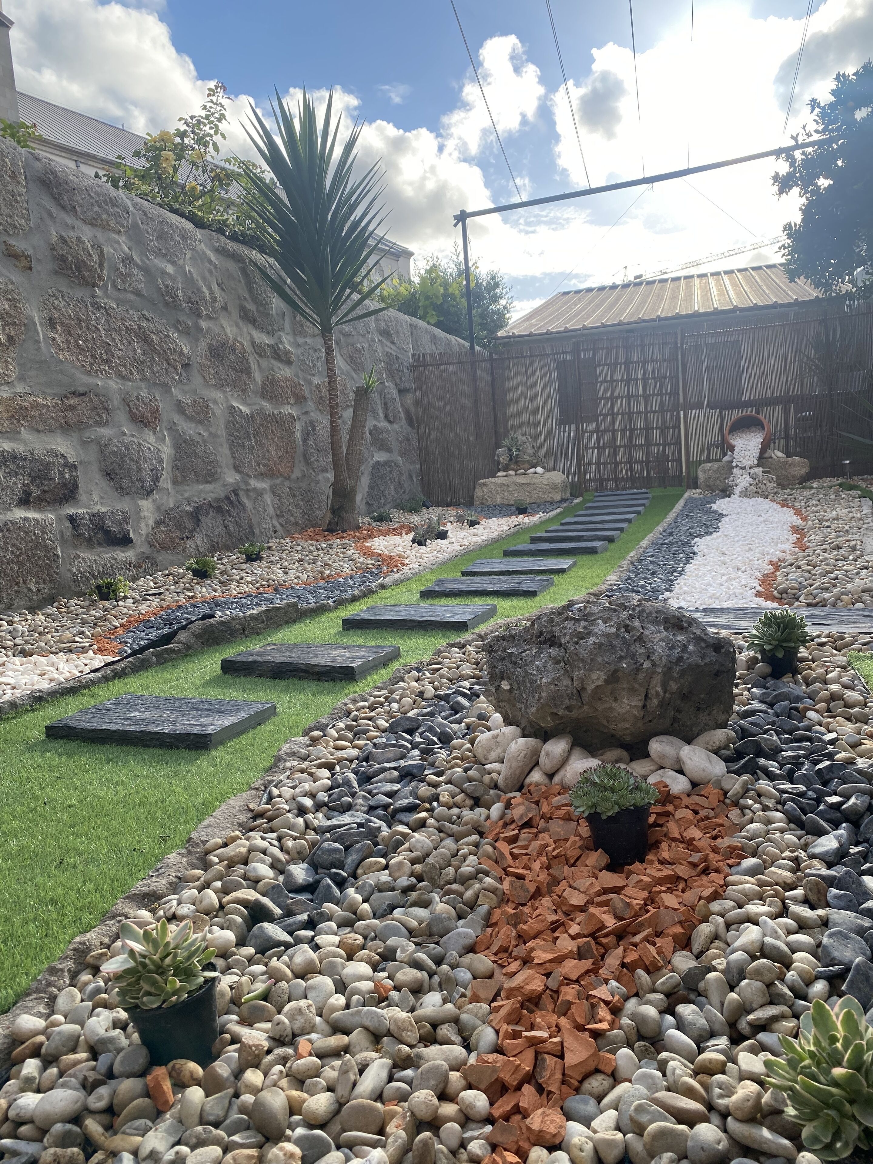 Un jardin avec un mur en pierre, une clôture en bois et un sentier bordé de pierres plates servant de pas.