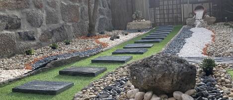 Un jardin avec un mur en pierre, une clôture en bois et un sentier bordé de pierres plates servant de pas.
