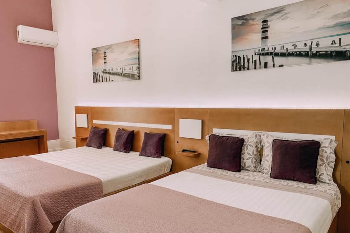Habitación de hotel con dos camas, cabecero de madera y obras de arte en las paredes.