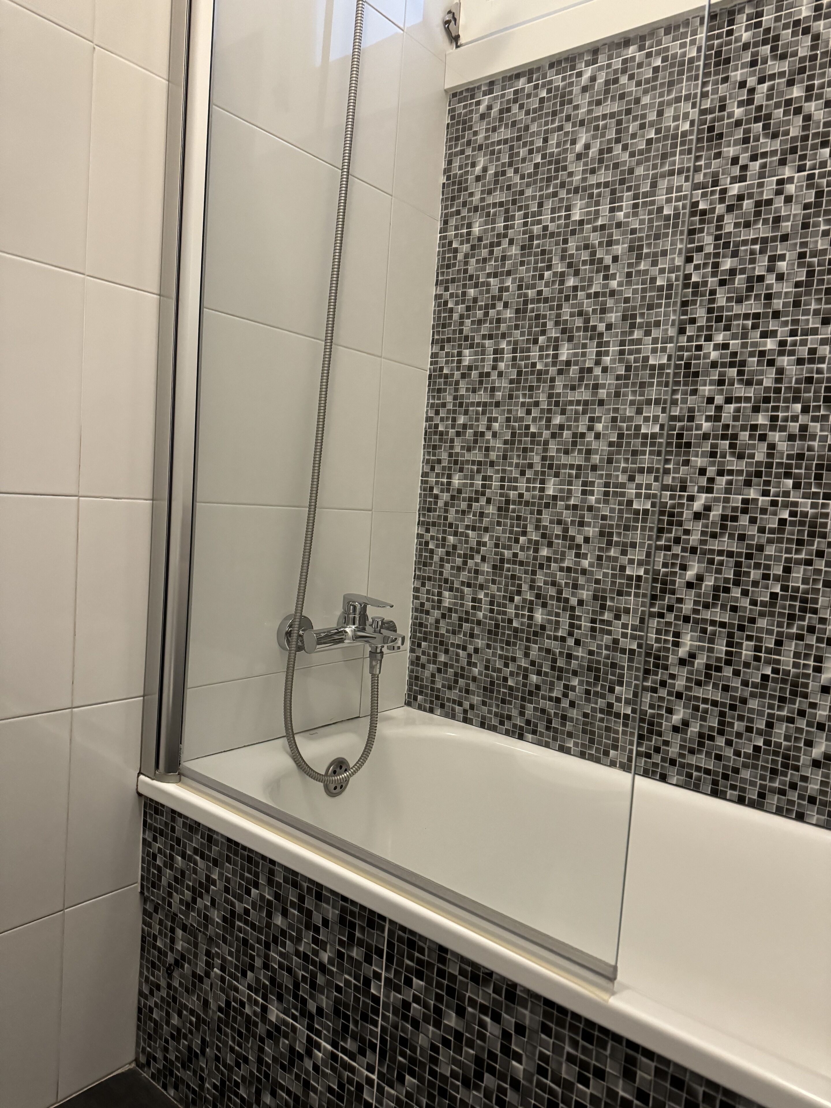 A modern shower area with a glass enclosure, a chrome showerhead, and a tiled mosaic wall.