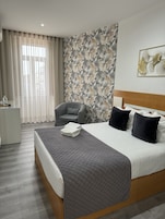 Una habitación de hotel con cama, una silla, un escritorio y un ventanal con cortinas.