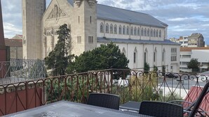 A terrace with a table and chairs, overlooking a historic building with a tall tower and a smaller adjacent structure. - GuestHouse do Marquês (Porto)