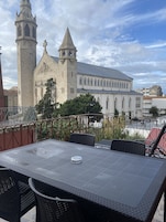 A terrace with a table and chairs, overlooking a historic building with a tall tower and a smaller adjacent structure.