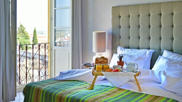 A hotel room with a bed, breakfast tray, and a view of the city through a balcony. - Noble House Essence Évora - by Unlock Hotels (Évora)