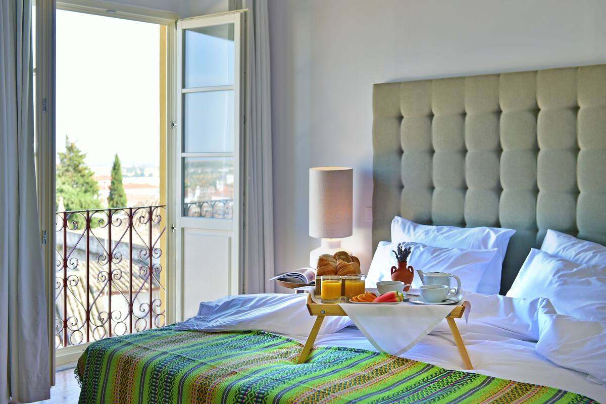A hotel room with a bed, a breakfast tray with croissants, orange juice, and a cup of coffee.