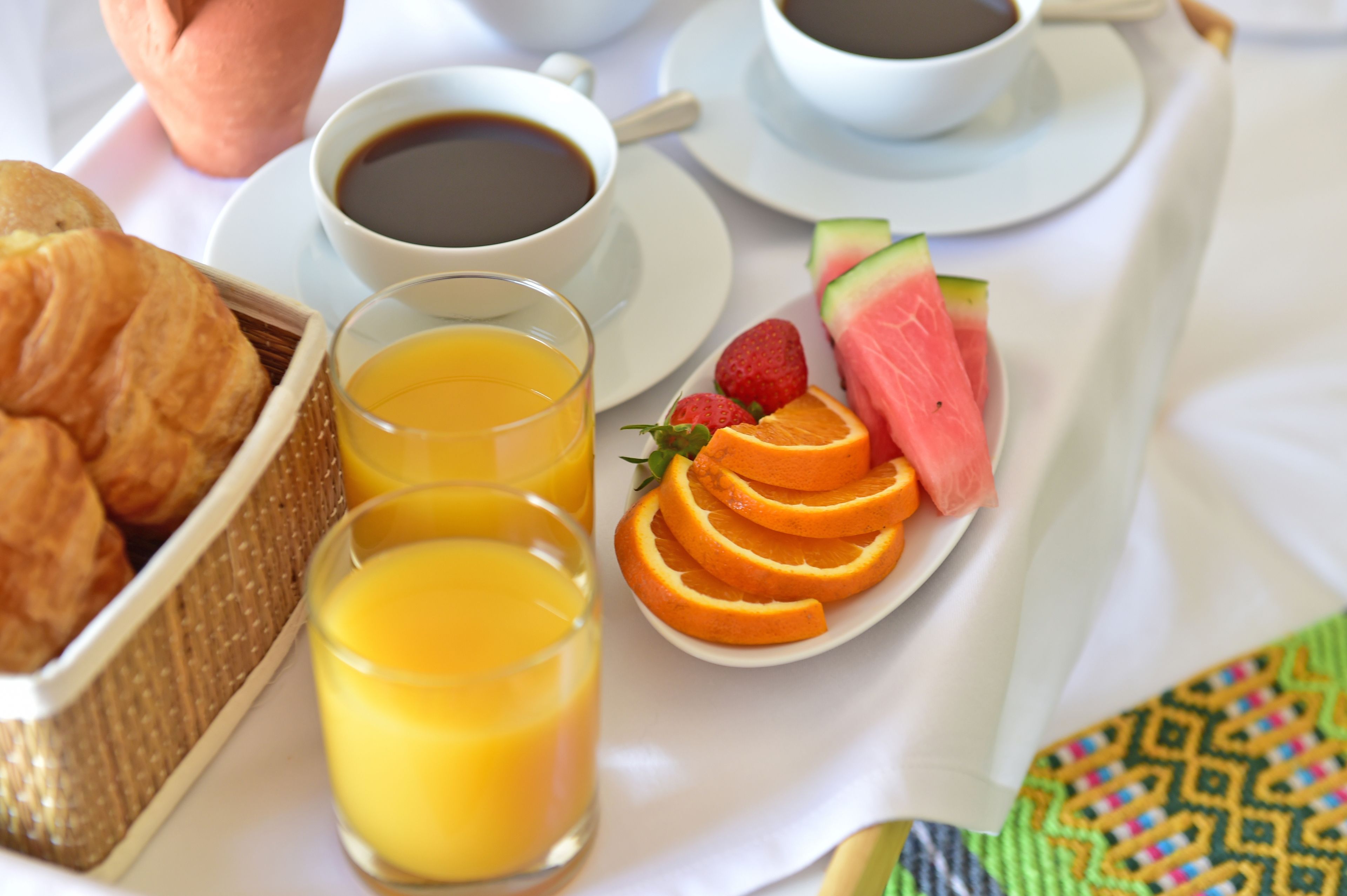 A breakfast setting with croissants, orange juice, coffee, strawberries, watermelon, and a napkin.