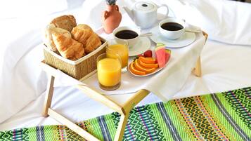 A breakfast setup on a bed with croissants, orange juice, coffee, and fresh fruits.