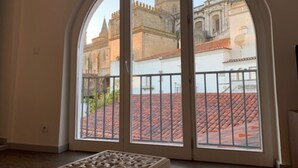A room with a large arched window offering a view of a historic building with a tower. - Noble House Essence Évora - by Unlock Hotels (Évora)