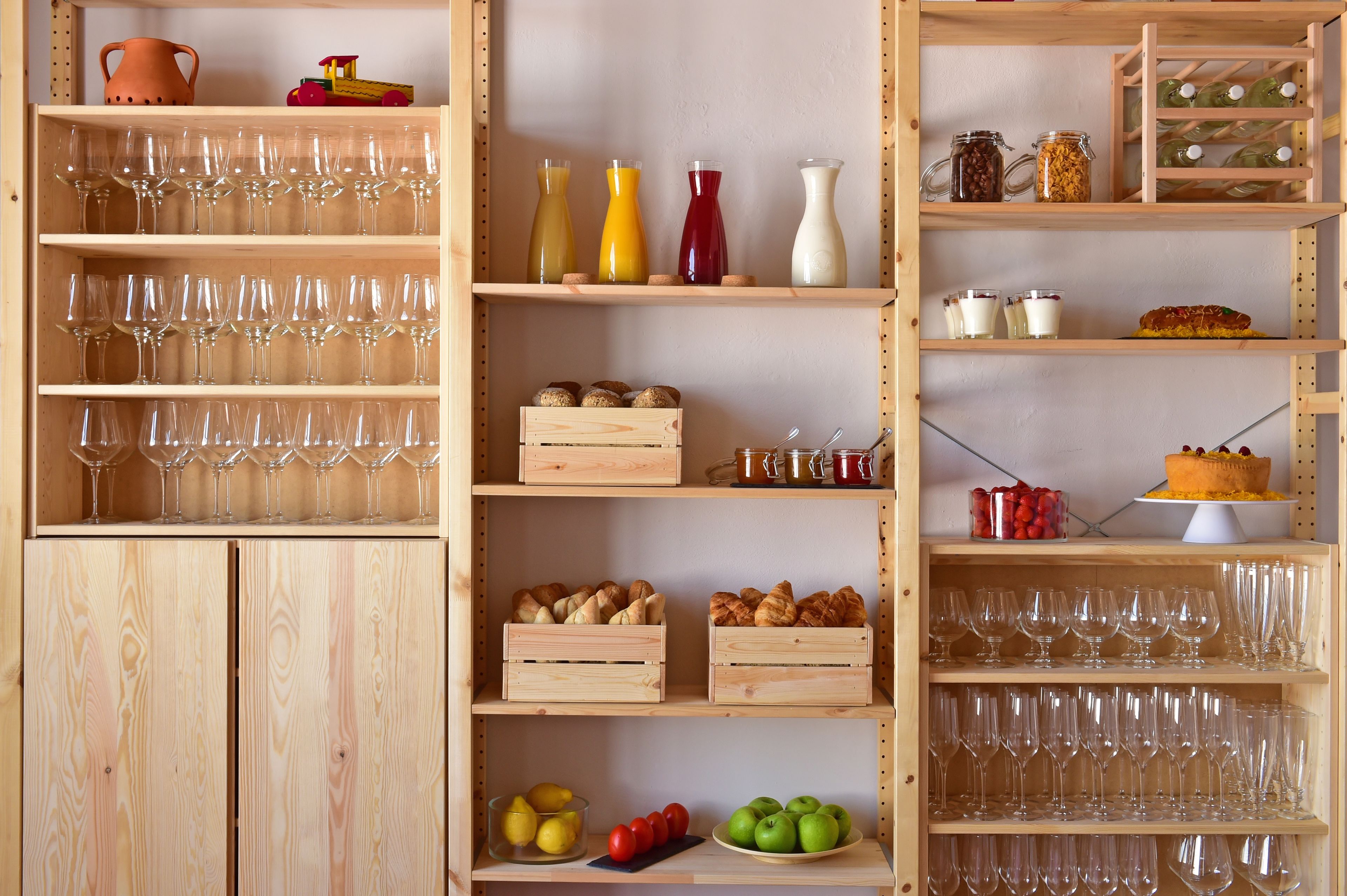 A wooden wine rack with multiple shelves holding wine glasses, jars, and a cake.