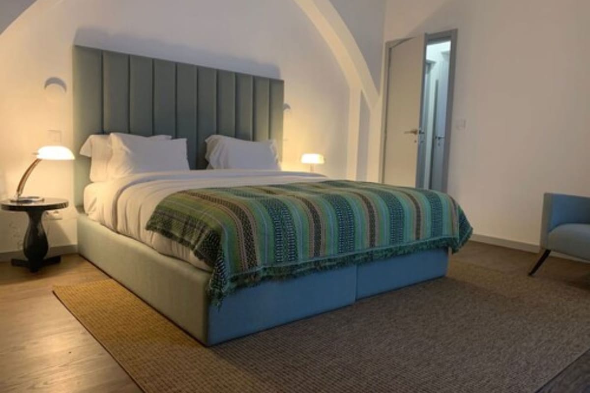 A bedroom with a bed, two bedside lamps, a door, and a chair.