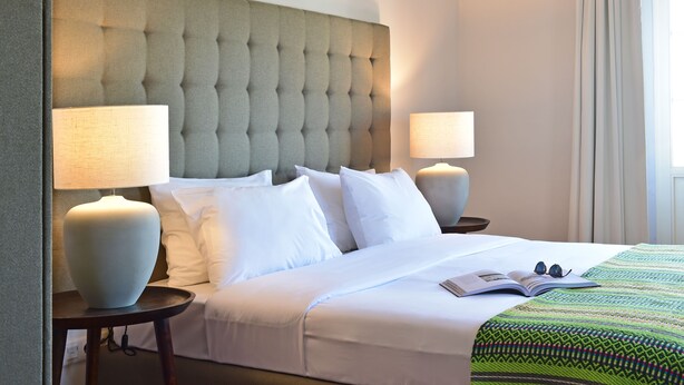 A neatly made bed with white linens, two bedside lamps, and a green patterned throw blanket. - Noble House Essence Évora - by Unlock Hotels (Évora)