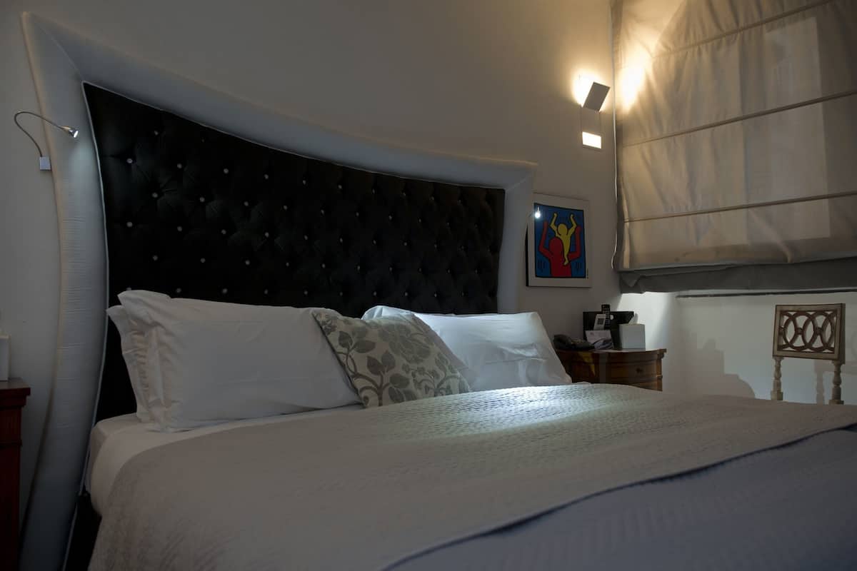 A neatly made bed with a tufted headboard, a bedside table with a lamp, and a wall-mounted light fixture.