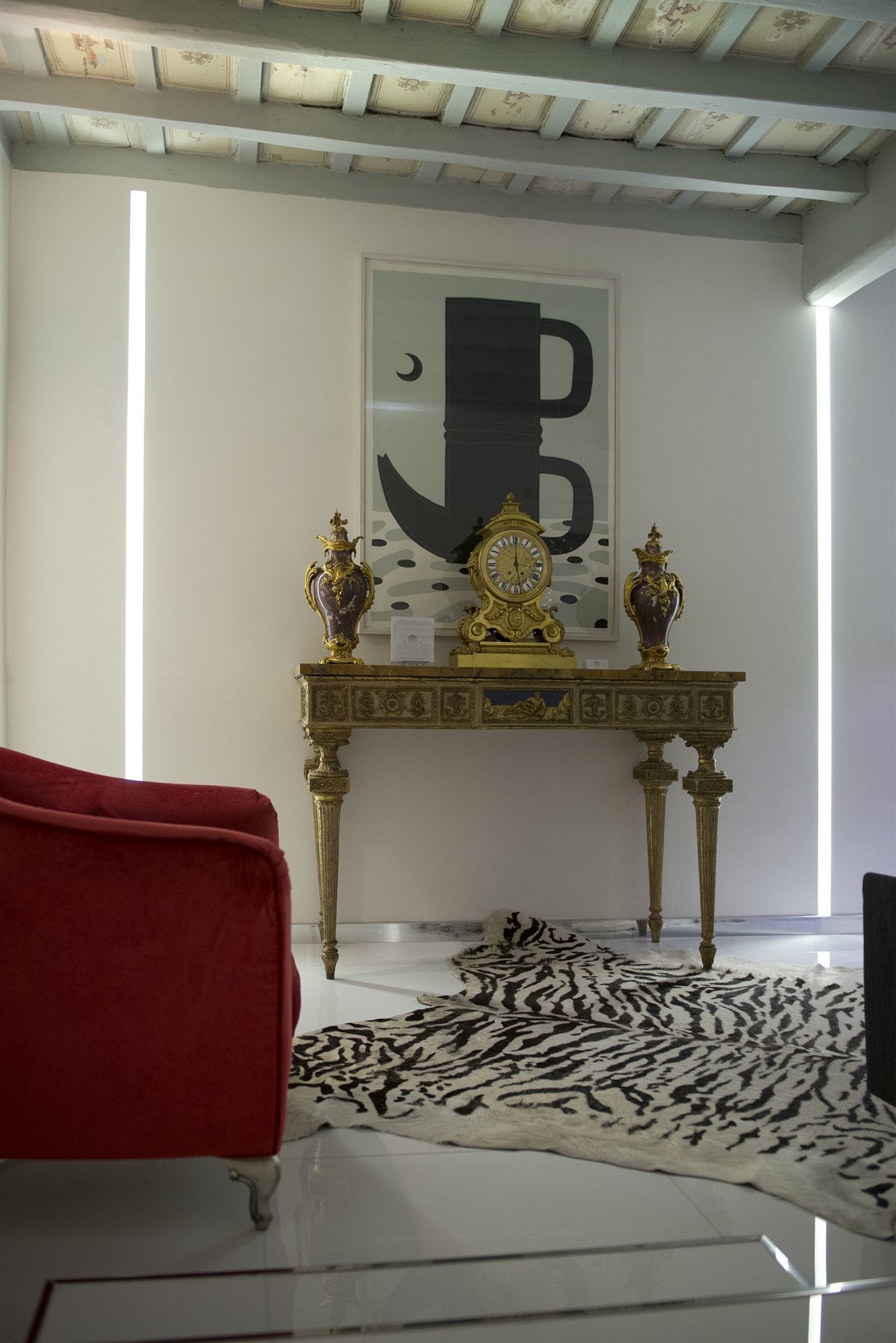 Habitació amb un sofà vermell, una catifes amb dibuixos, una taula decorativa amb dos vasetes i una paret amb una lletra 'B' gran i un disseny de lluna creixent.