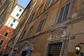 A narrow street with historic buildings, including a building with a lion relief and a shop with a blue sign. - Pantheon Relais (Rome)
