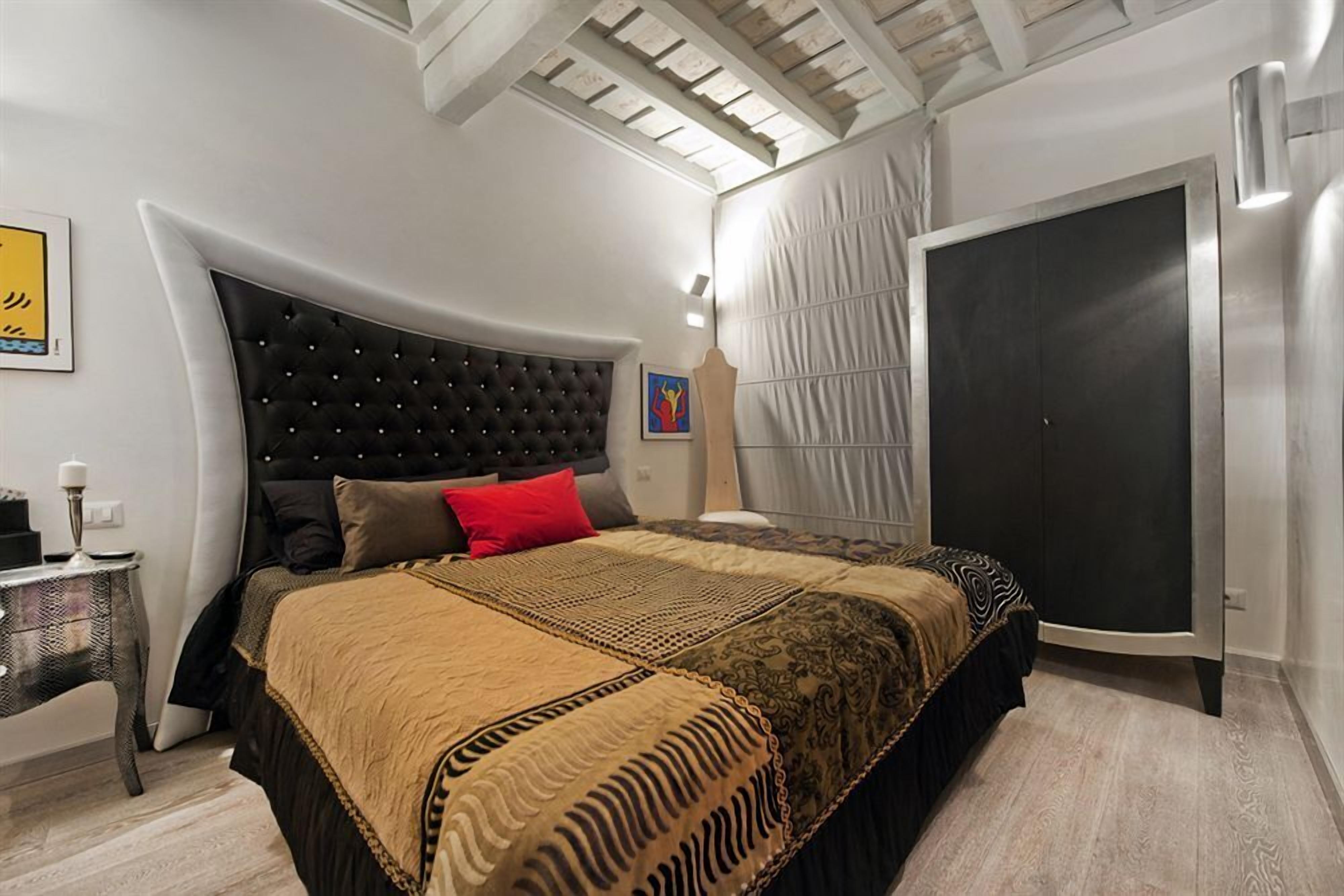Un dormitorio moderno con un cabecero capitonado, una cama grande con ropa de cama estampada, un armario y una mesita de noche.