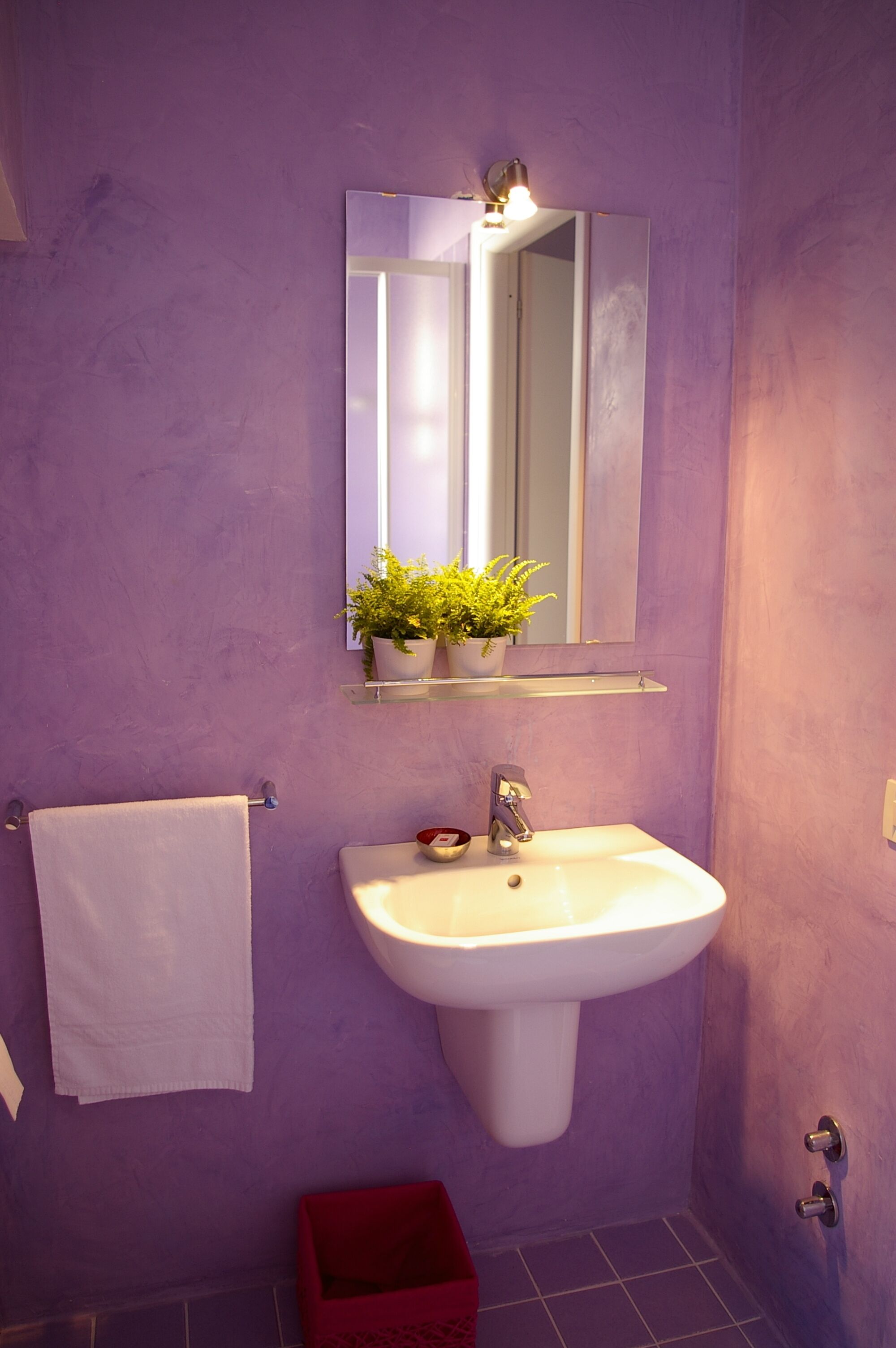 Une salle de bain avec un mur violet, un lavabo blanc, un miroir et un porte-serviettes.