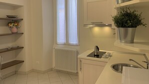 Una cocina moderna con armarios blancos, horno empotrado, lavamanos y ventana con cortinas.