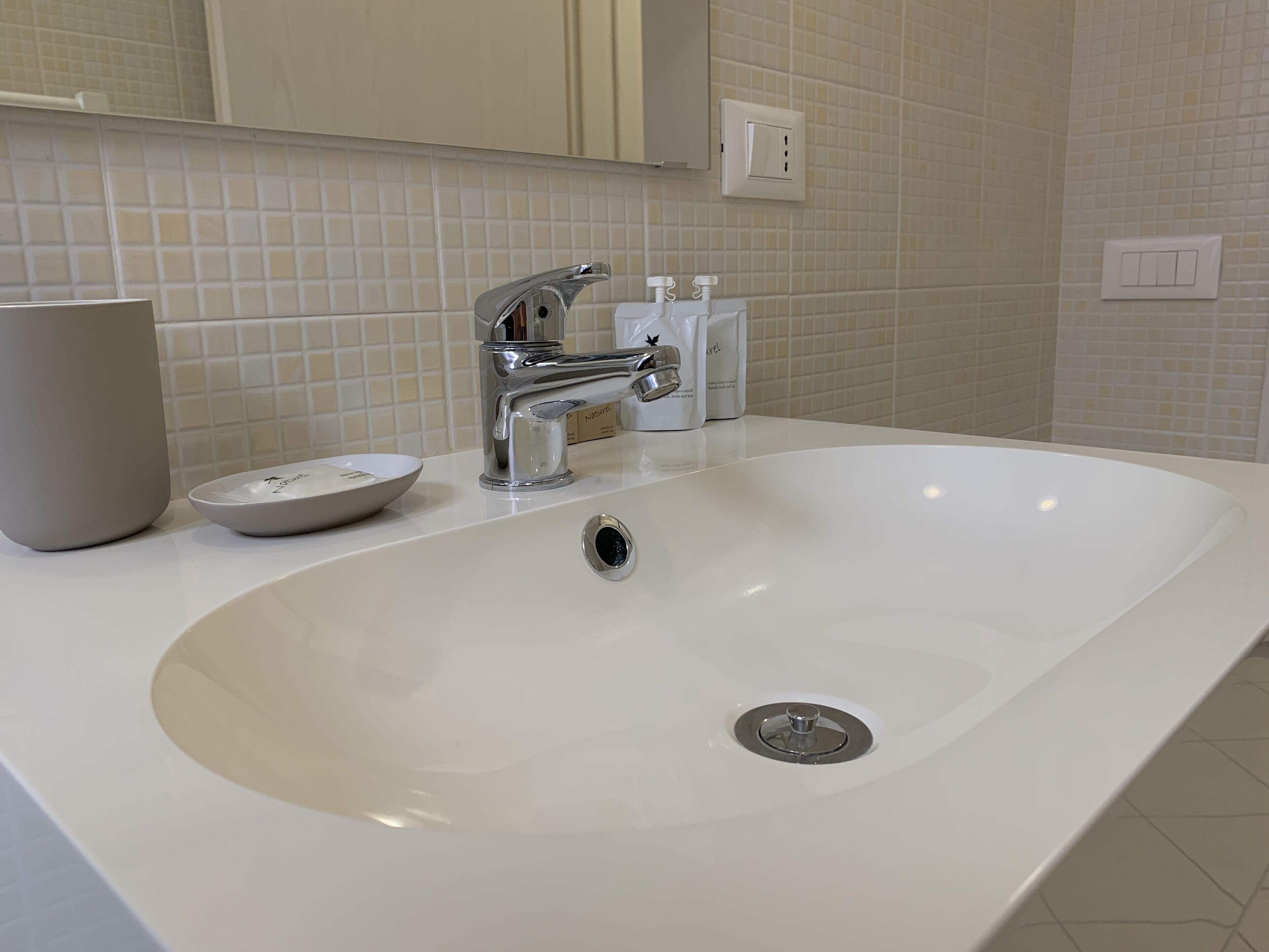 Een moderne badkamer met een witte wastafel, een chromen kraan en een spiegel erboven.