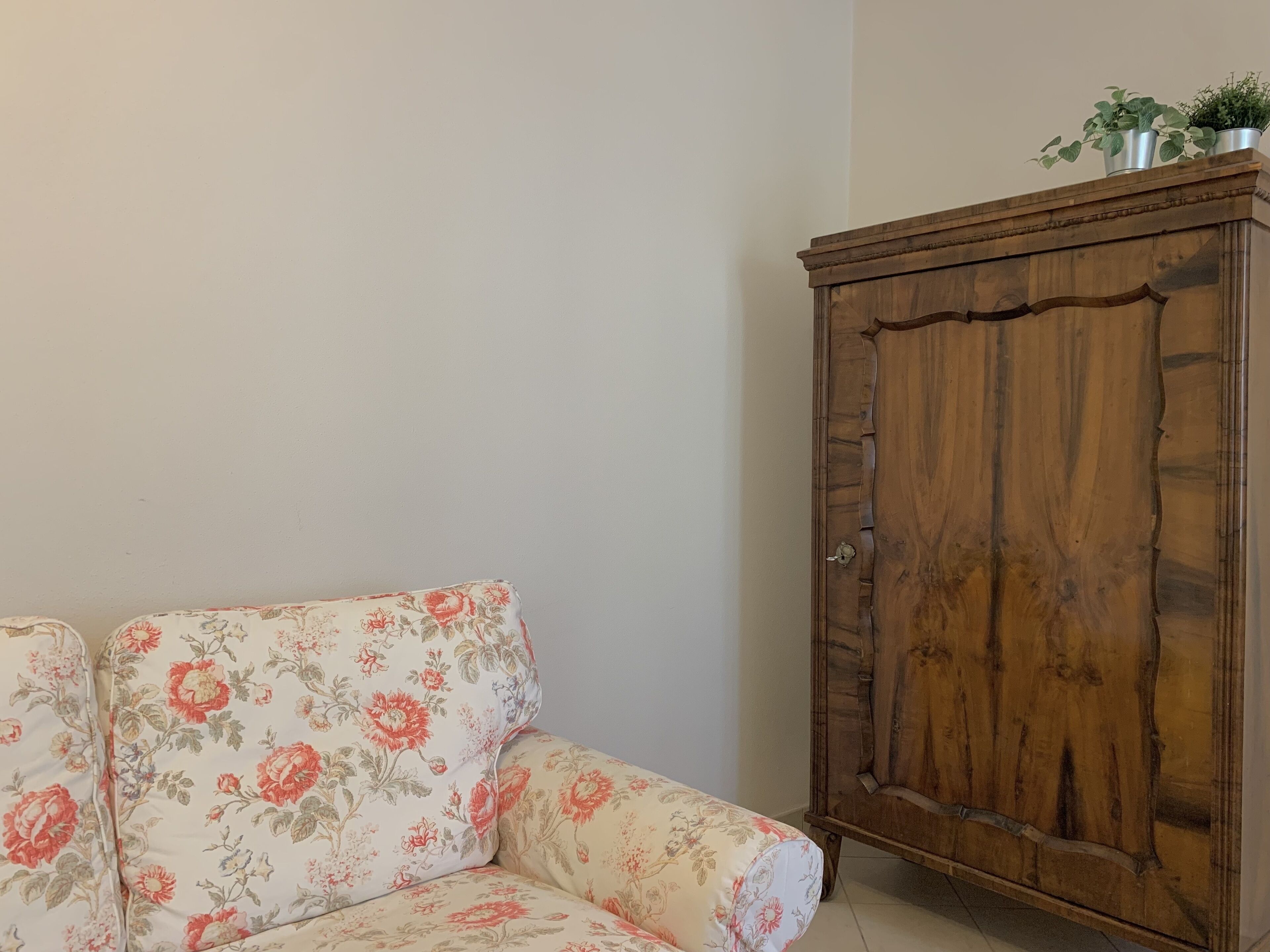 A floral sofa and a wooden cabinet against a plain wall.