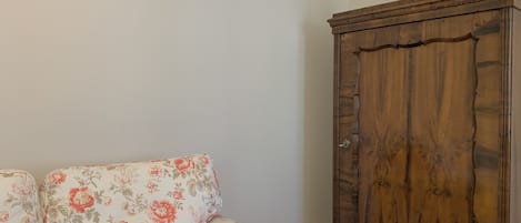 Un sofá floral y un aparador de madera frente a una pared lisa.