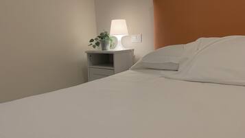 A neatly made bed with white linens, a bedside lamp, and a small potted plant on a white nightstand.