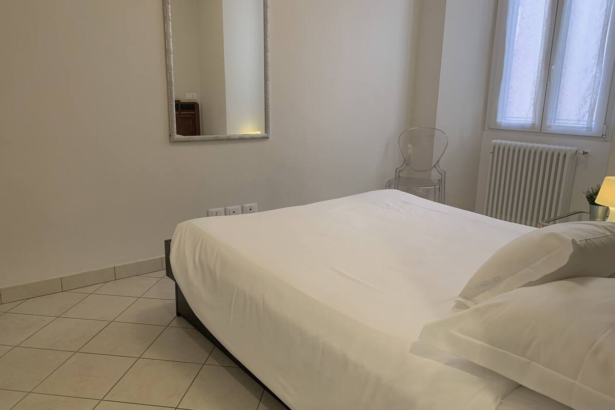 Une chambre à coucher avec un lit, un miroir, un radiateur et une fenêtre.