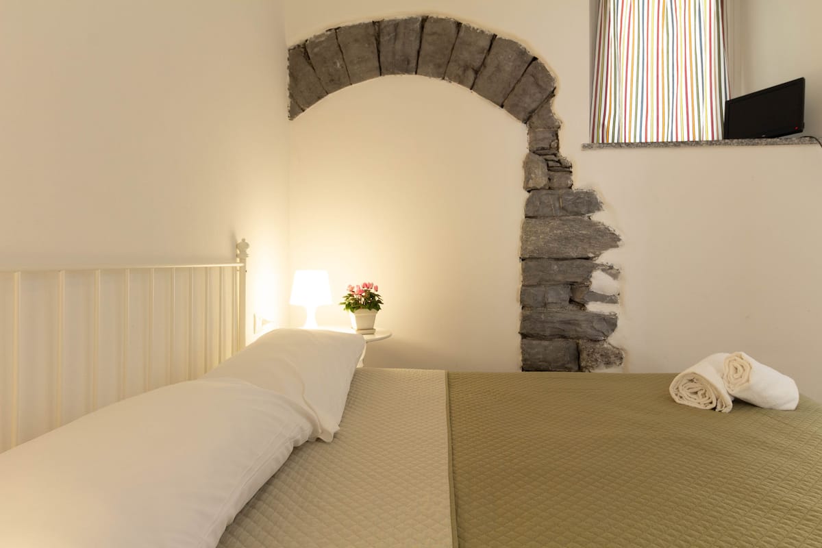Une chambre à coucher avec un lit, une table de chevet avec une lampe, une plante en pot et une arche en pierre.