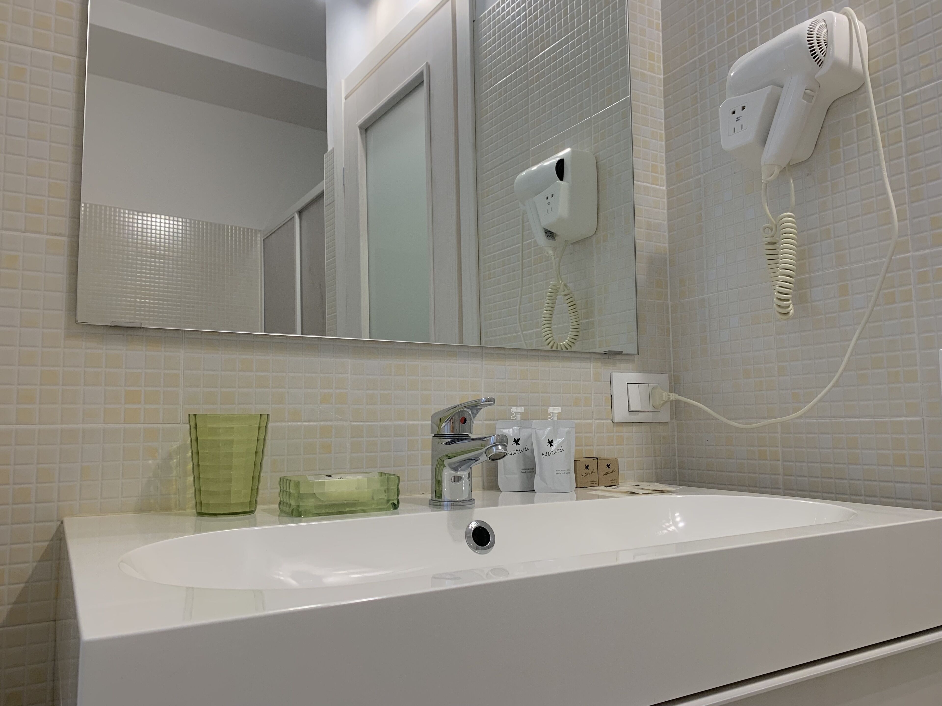 A bathroom with a white sink, a mirror, a hairdryer, and toiletries on the counter.